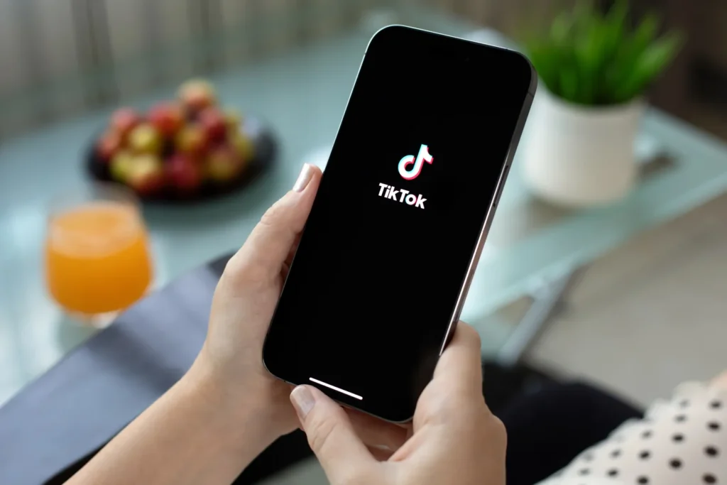 Kobieta trzyma smartfon z ekranem startowym aplikacji TikTok