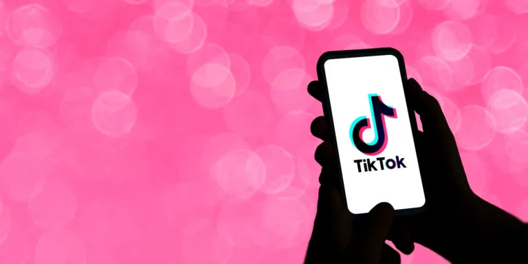 Sylwetka dłoni z telefonem z logo TikTok na różowym tle — twórca w programie partnerskim