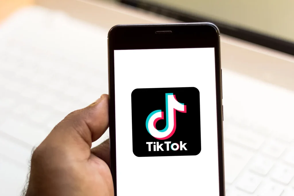 Dłoń trzyma smartfon z ikoną aplikacji TikTok na białym ekranie
