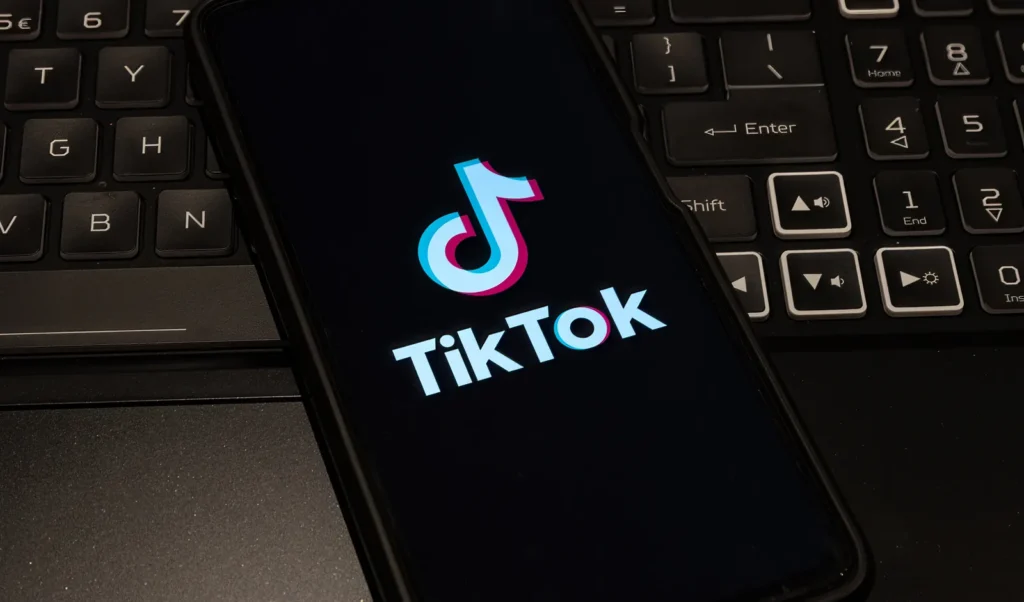 Smartfon z logo TikTok leżący na klawiaturze komputera — praca z panelem reklamowym