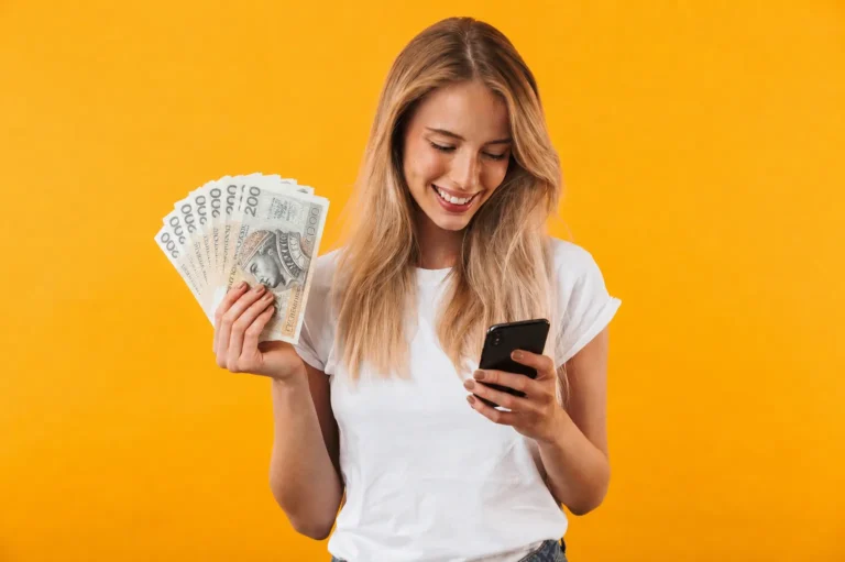 Uśmiechnięta kobieta trzyma banknoty i smartfon — zarobki z TikToka wypłacone na konto
